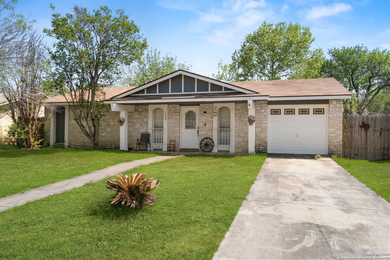 Single-story stone-front house with an attached garage, covered entry, and broad concrete driveway.