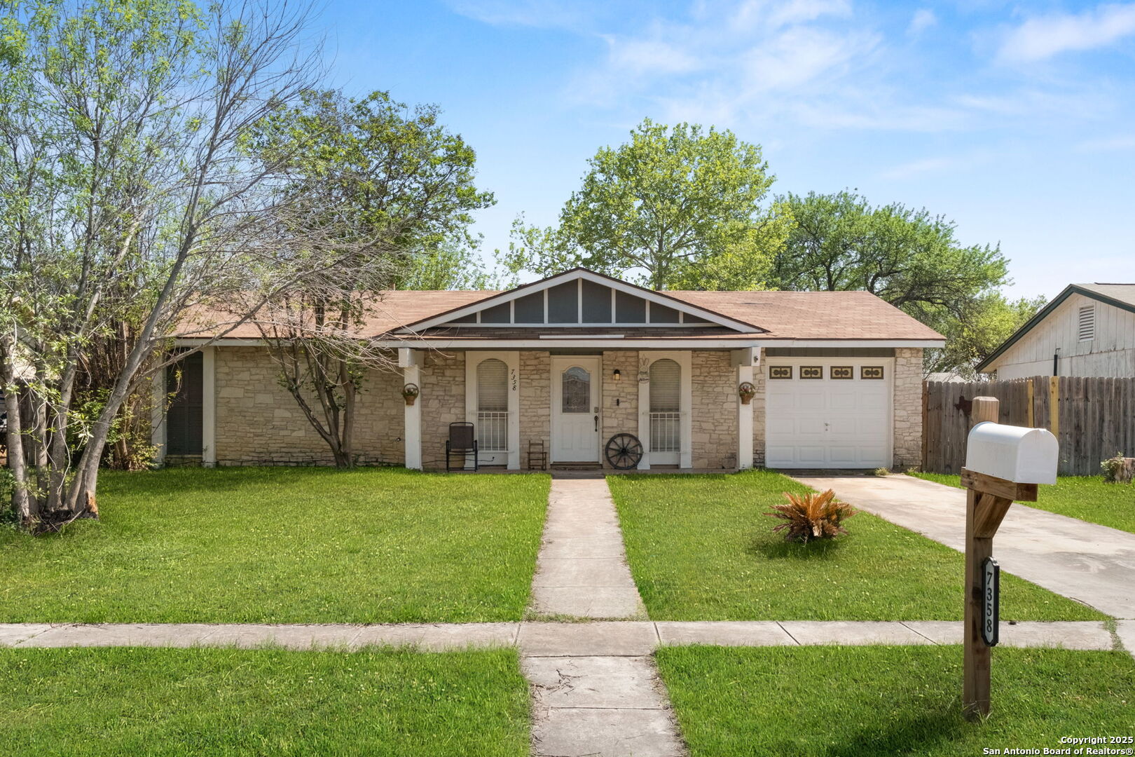 Single-story stone-front house with a covered porch, attached garage, and mailbox marked 7358.