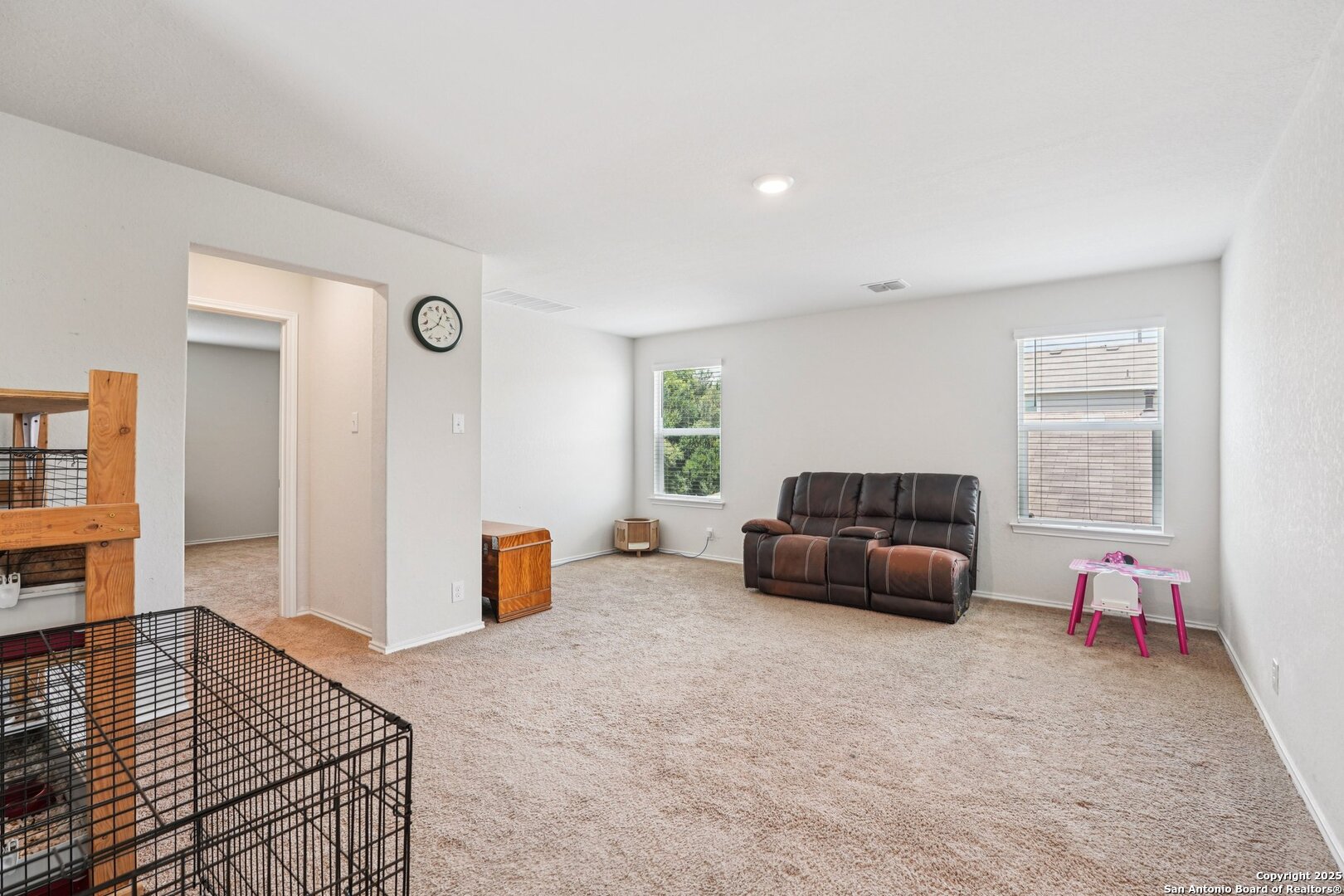 Living room with a dark reclining sofa, beige carpet, and a small pink children's table.
