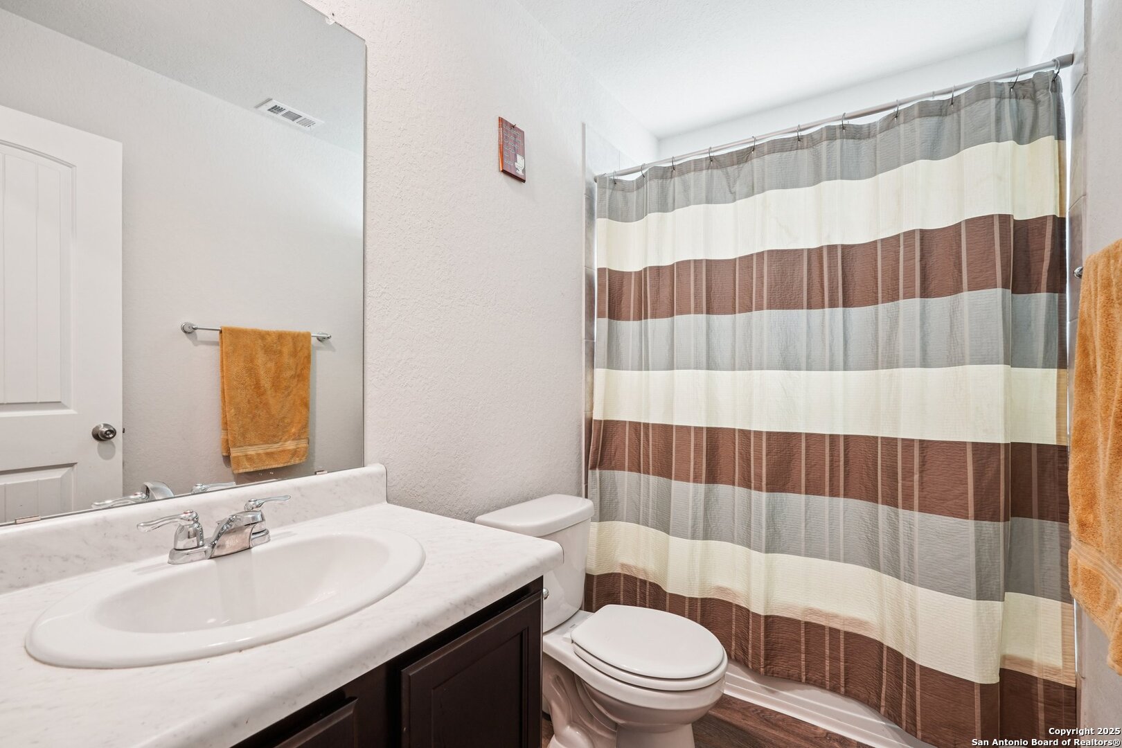 Bathroom with a marble-look vanity, white sink, toilet, and striped shower curtain.