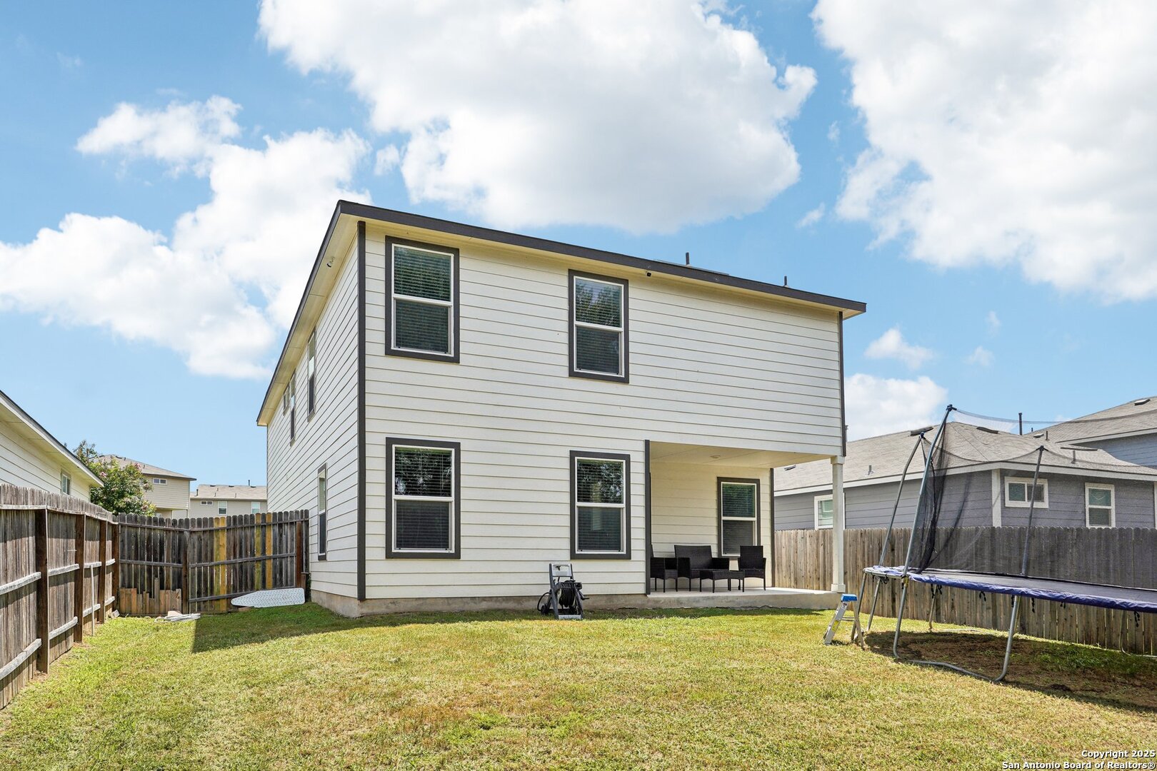 Two-story white house with a covered patio, fenced lawn, and backyard trampoline.