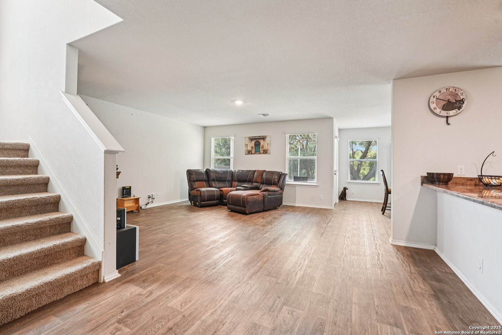 Living room with brown leather sectional, wood-look floors, and a carpeted staircase.