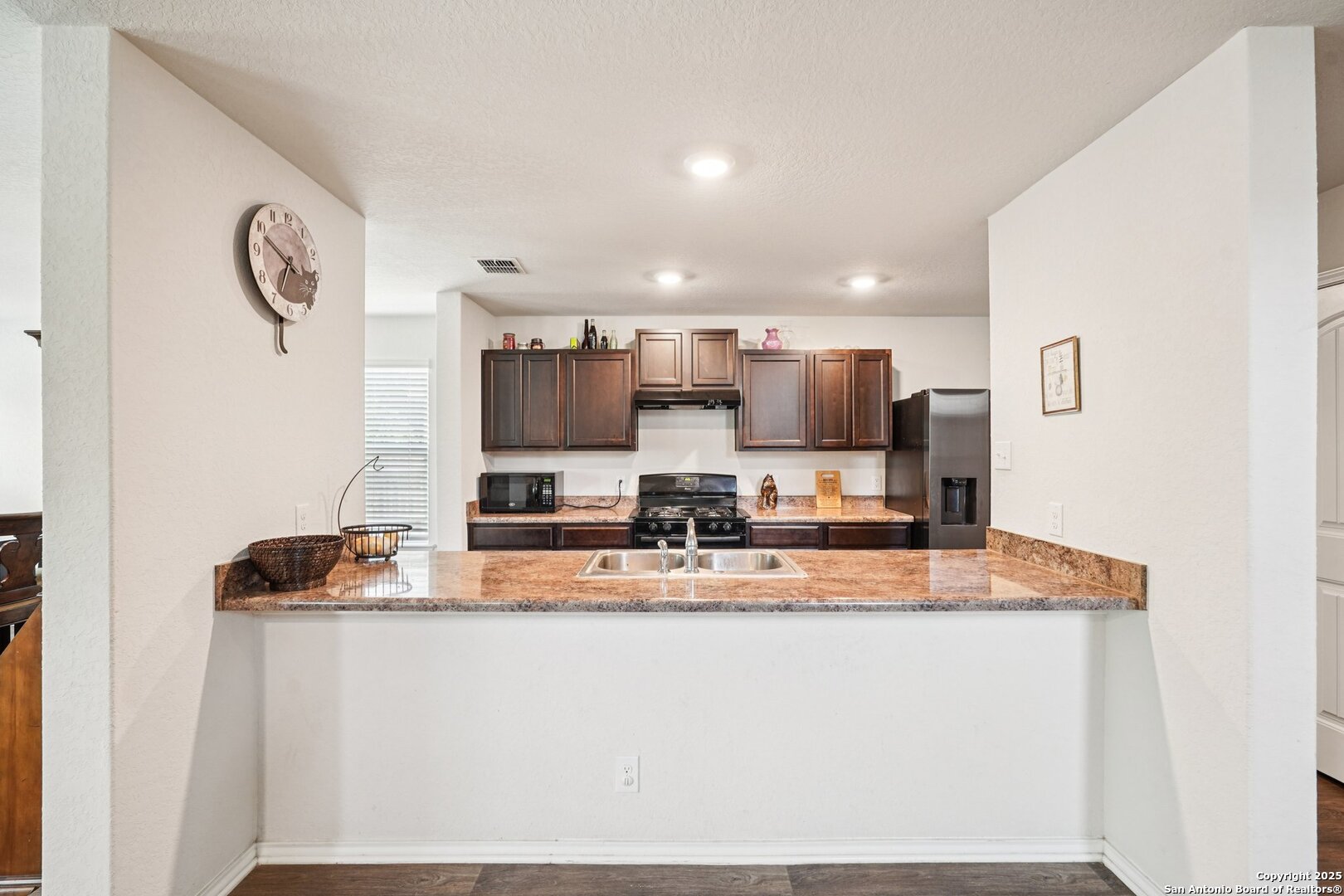 Kitchen with dark wood cabinets, stainless steel appliances, and a granite peninsula with a double sink.
