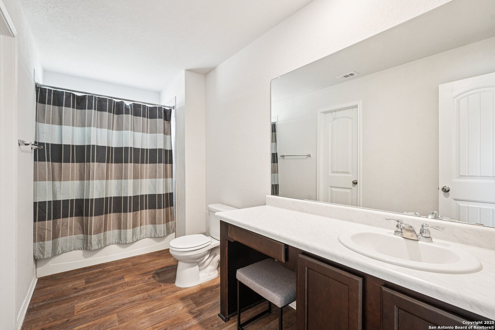 Bathroom with a striped shower curtain, bathtub, and dark wood vanity beneath a large mirror.