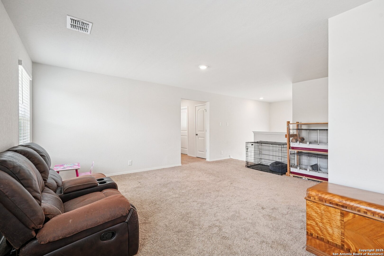 Carpeted living room with a brown reclining sofa and pet crates.