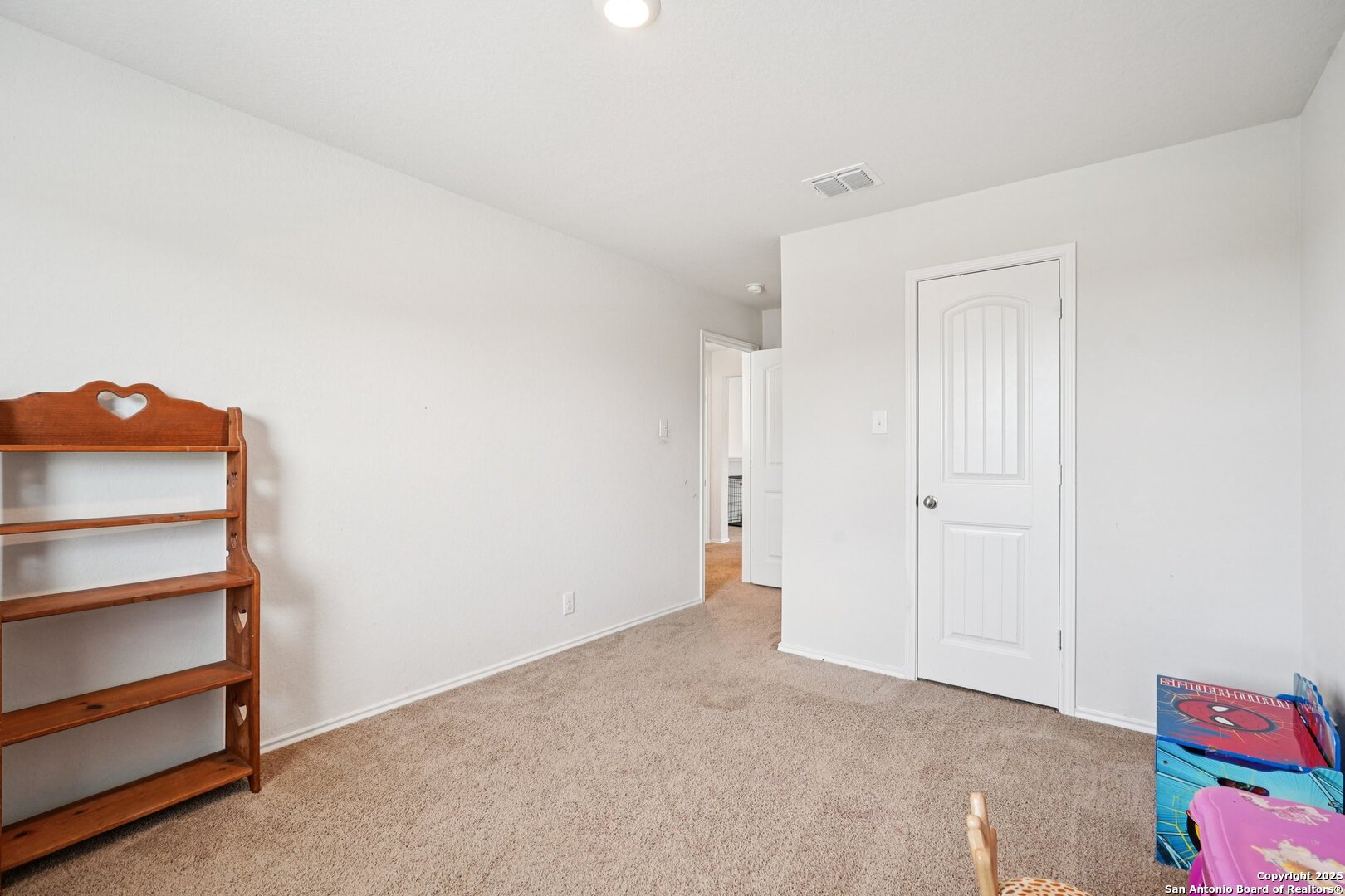 Carpeted bedroom with a wooden shelving unit, white paneled door, and toys at the edge of the frame.