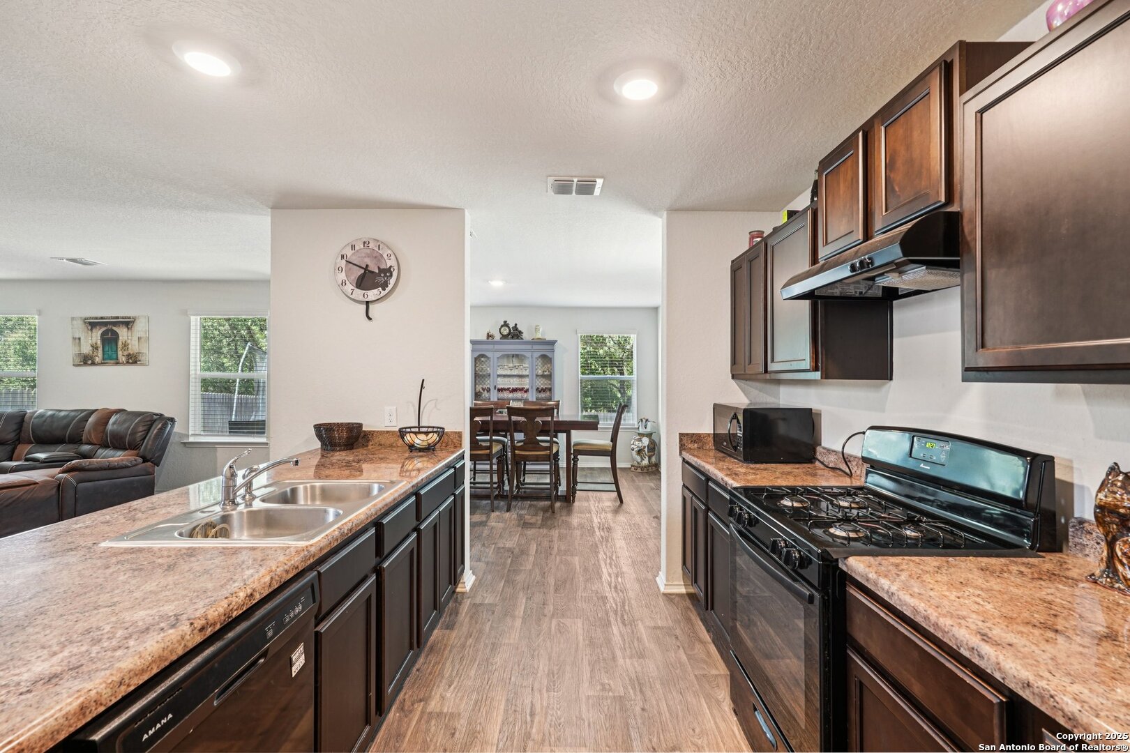 Kitchen with dark wood cabinets, granite-look counters, double sink, and gas range opening to the dining area.