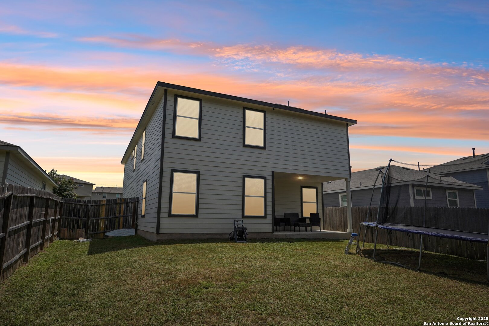 Two-story gray home with a covered patio and trampoline in the backyard at sunset.