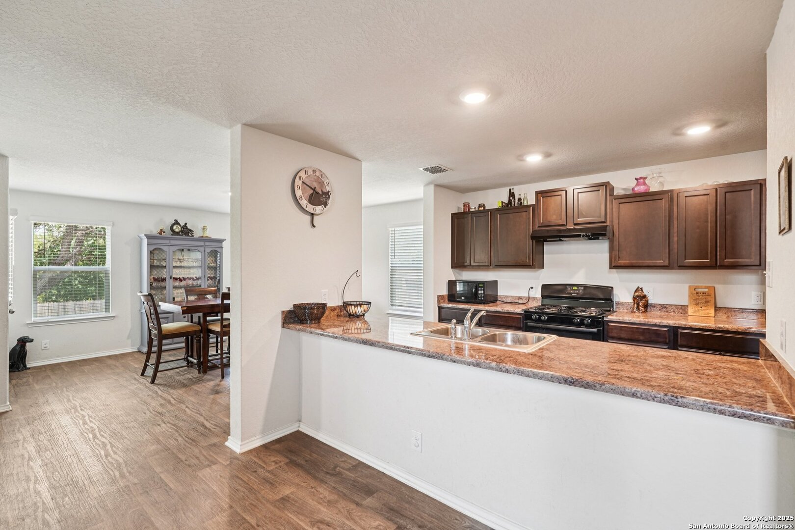 Kitchen with dark wood cabinets, a gas range, and a granite peninsula opening to a dining area.