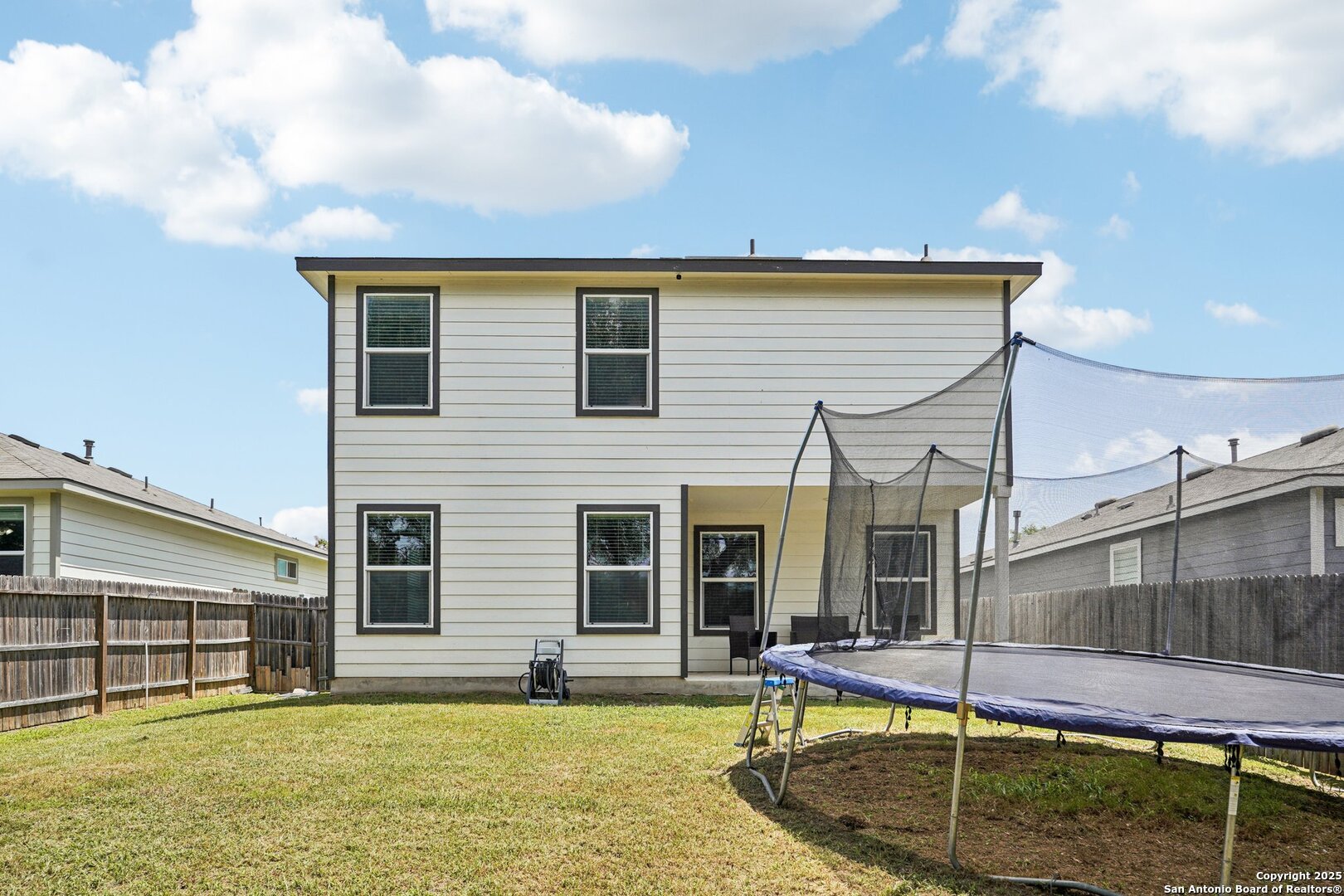 Two-story house viewed from the backyard, with a fenced lawn and large netted trampoline.