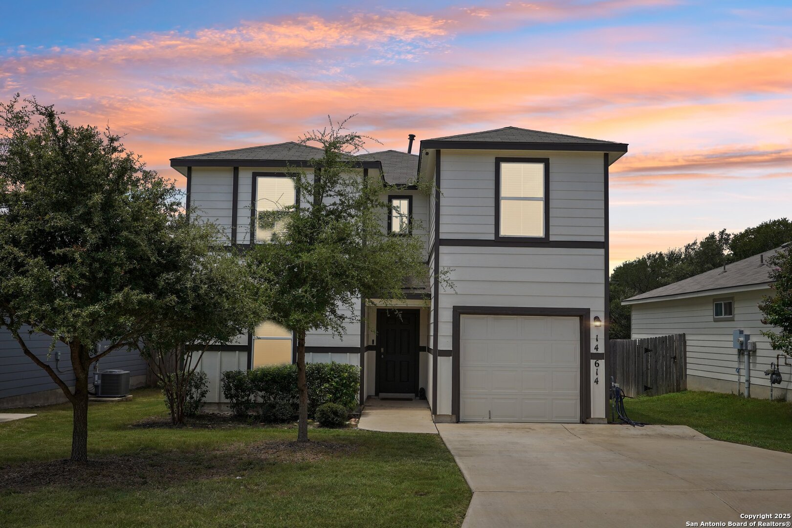 Two-story gray house with dark trim and an attached garage beneath a colorful sunset sky.
