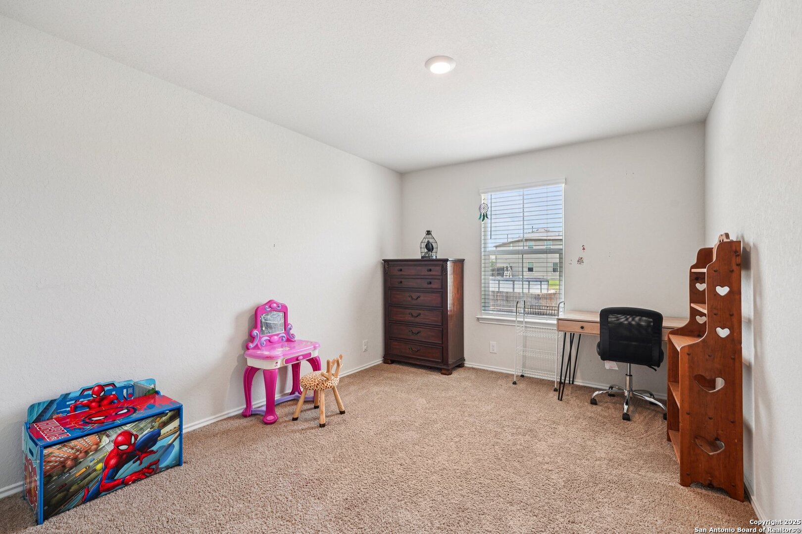Carpeted bedroom or study with a desk, wooden shelves, dresser, and children's toys.