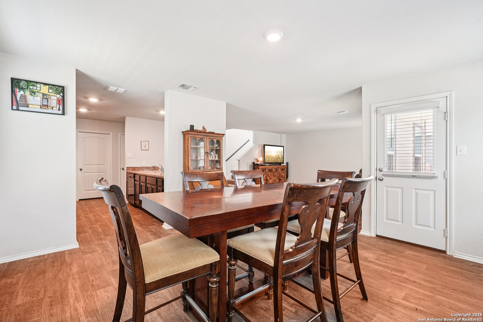 Dining area with a large wooden table, upholstered chairs, and wood-look flooring.