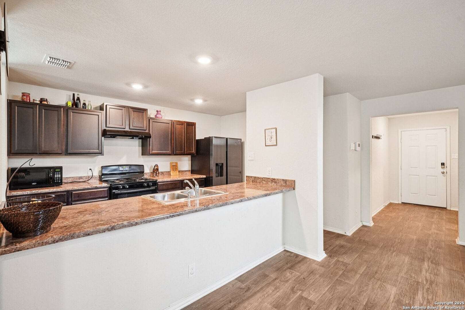 Kitchen with dark cabinets, granite counters, stainless appliances, and a breakfast bar opening toward the entry hall.