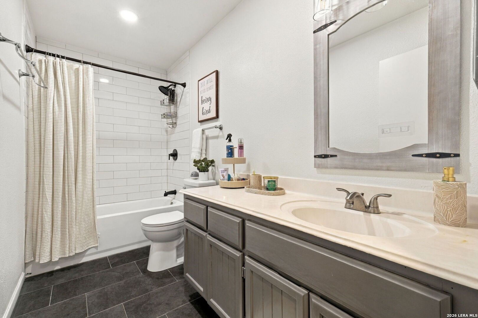 Bathroom with a subway-tile tub and shower, gray vanity, framed mirror, and dark tile floor.
