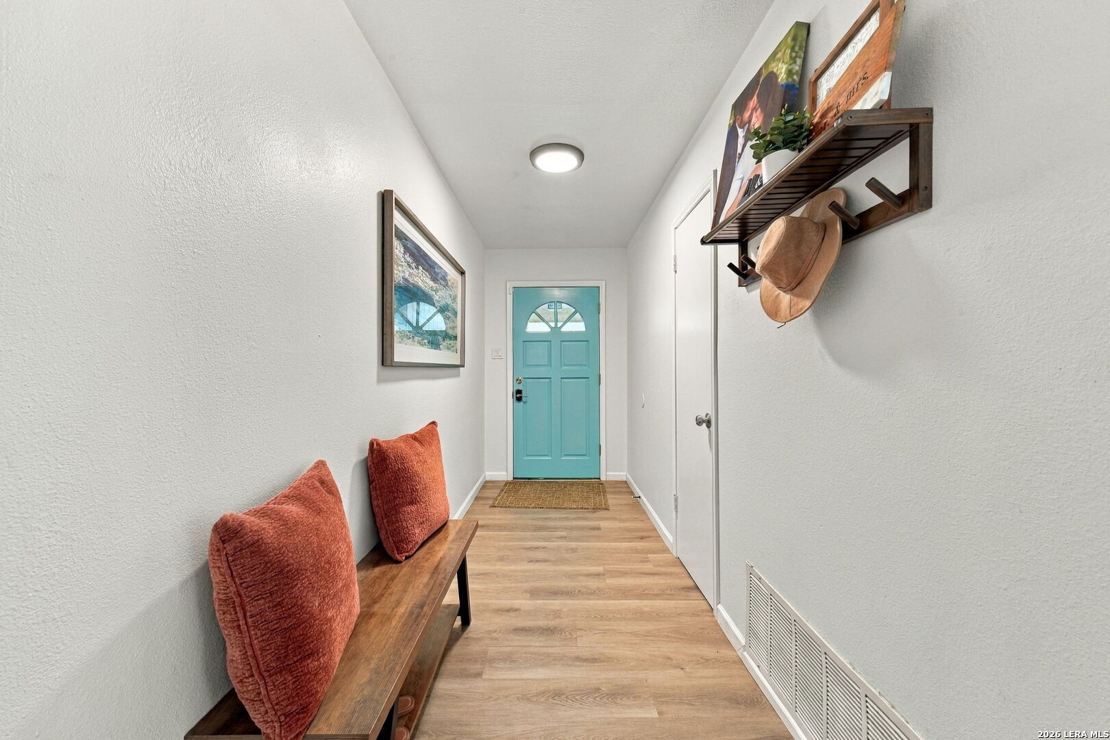 Entry hallway with a turquoise front door, wood-look flooring, and a bench with rust-colored cushions.