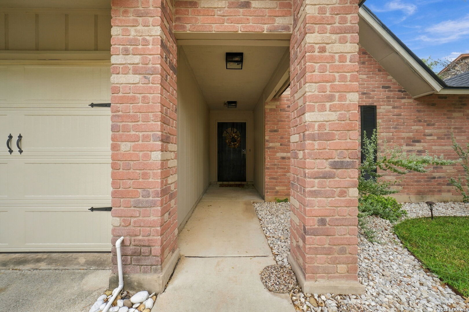Brick home’s covered entry with a walkway leading to a dark front door beside the garage.