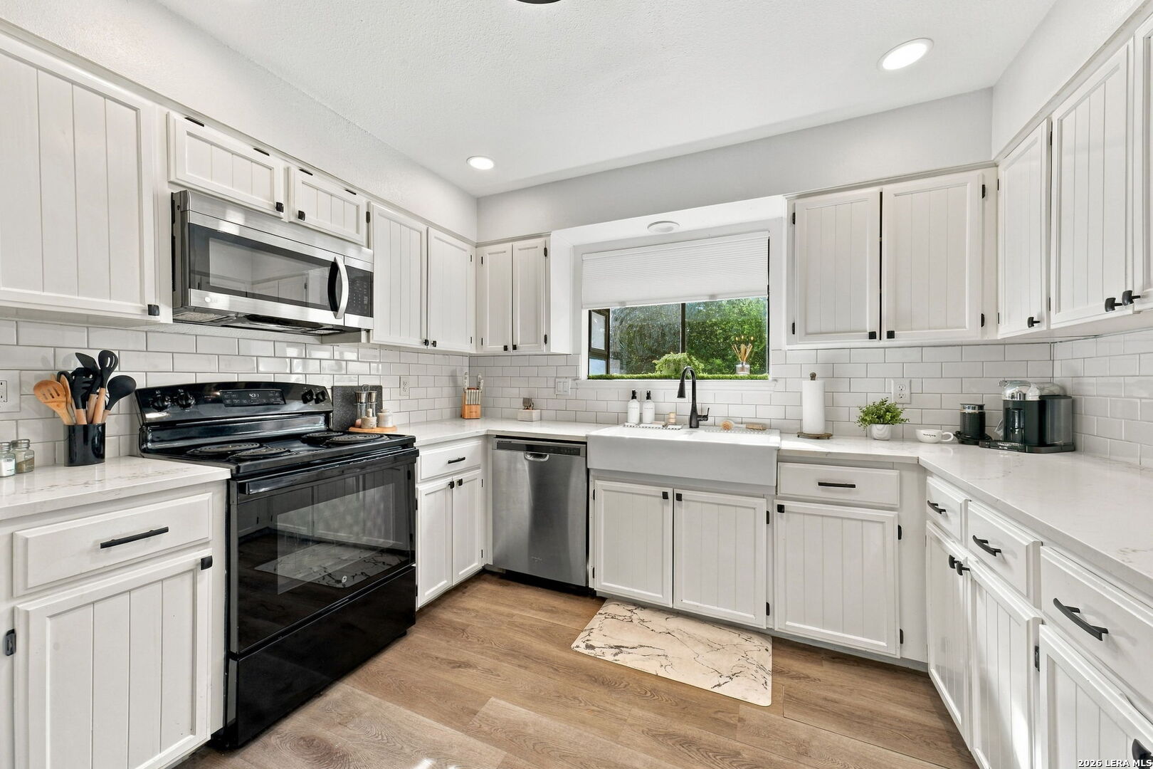 Bright white kitchen with a farmhouse sink, subway tile backsplash, and black range.