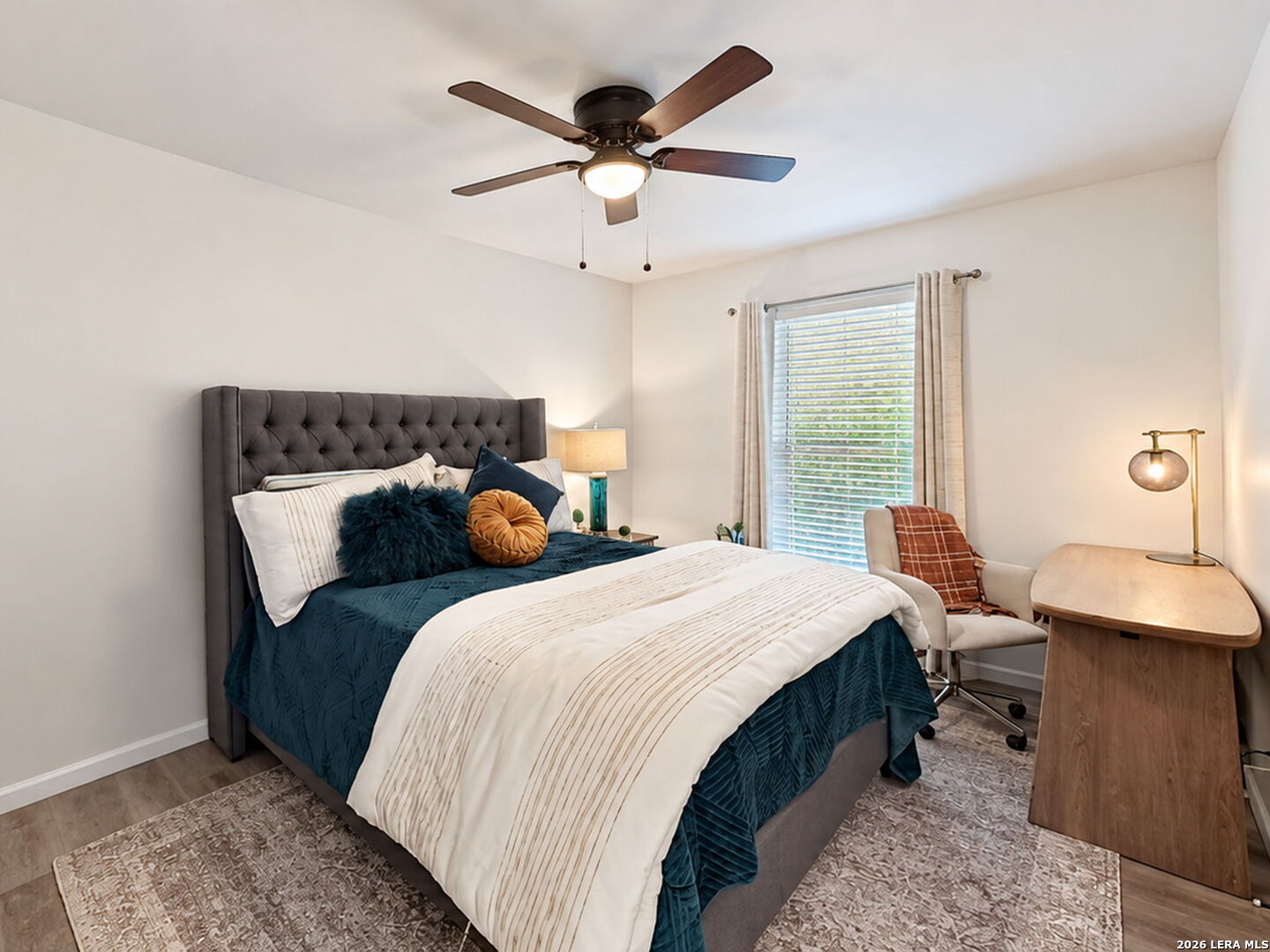 Staged bedroom with teal bedding, a tufted gray headboard, and a desk beside the window.