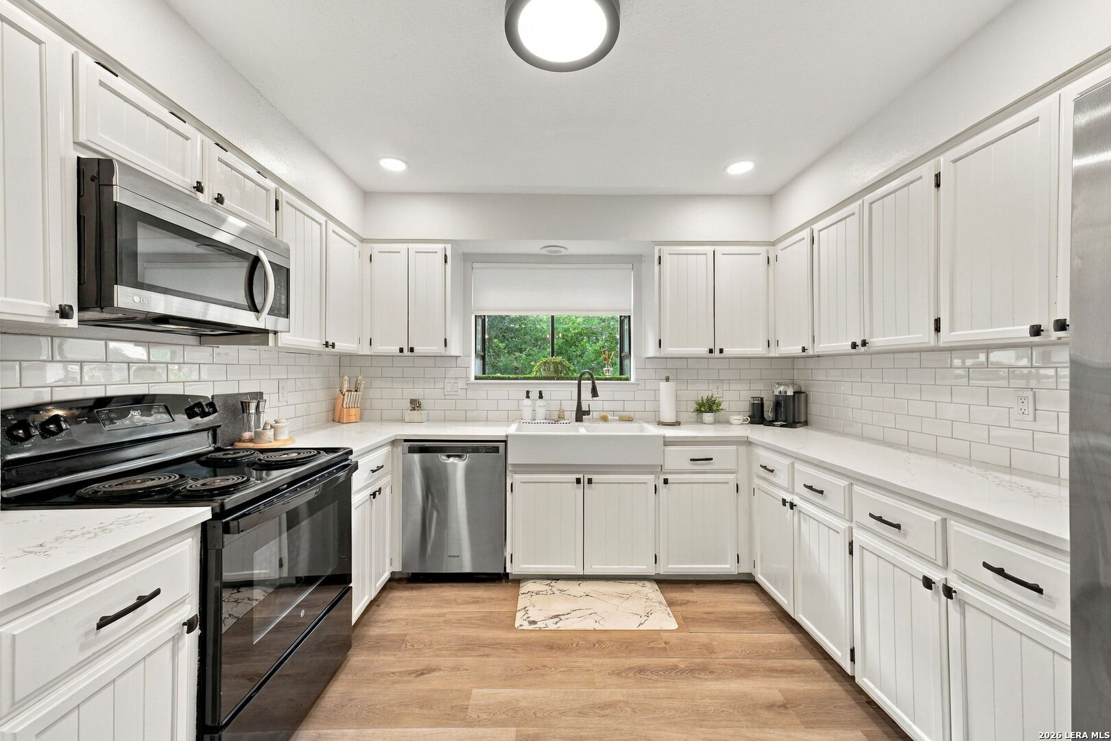 Kitchen with white shaker cabinets, farmhouse sink beneath a window, and black range and microwave.