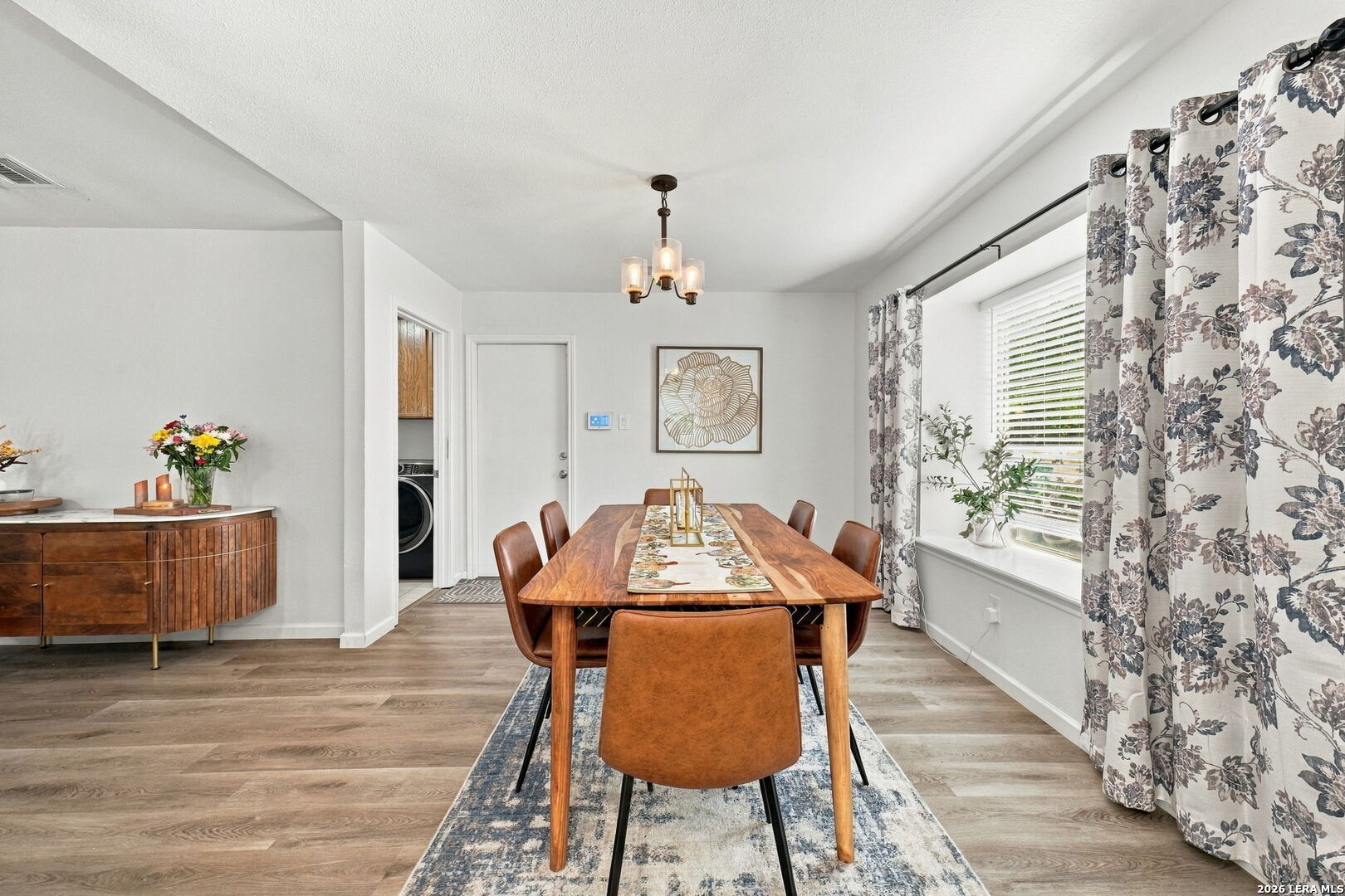 Dining room with a wooden table, leather chairs, patterned rug, floral curtains, and a sideboard.