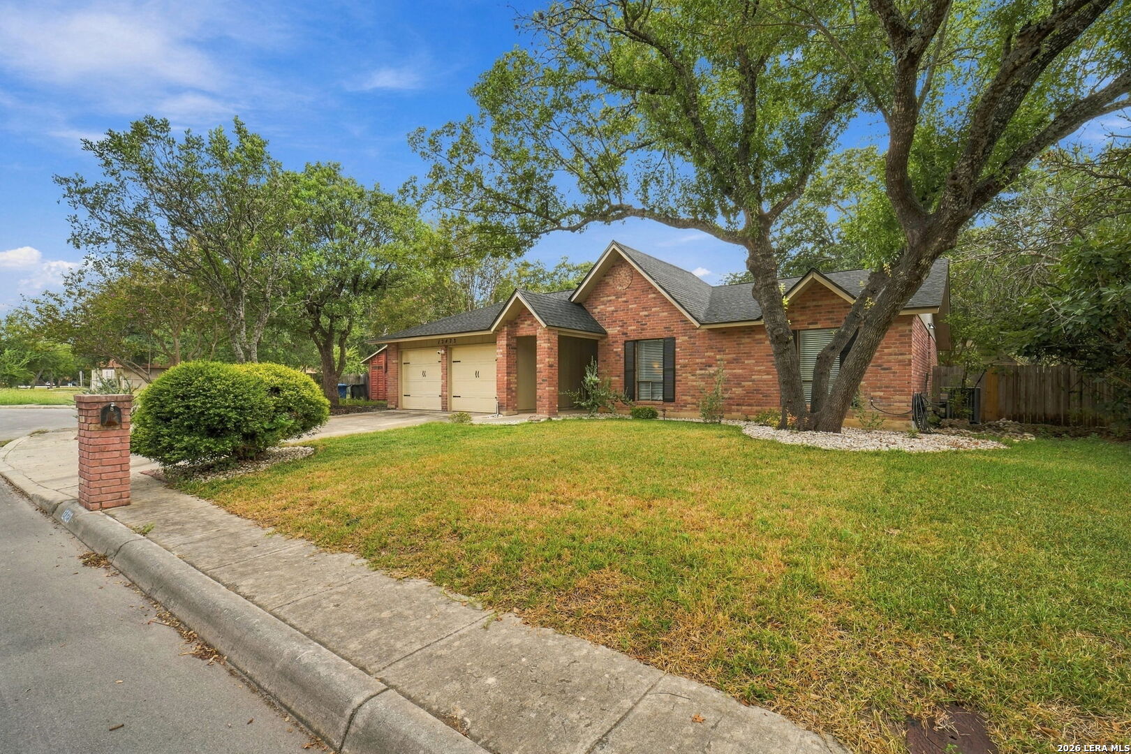 Red brick home with a two-car garage, broad lawn, and mature shade trees.