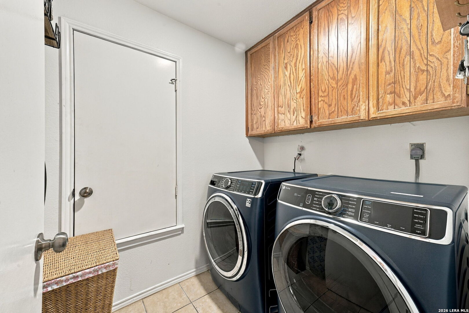 Laundry room with front-loading washer and dryer beneath wood cabinets.