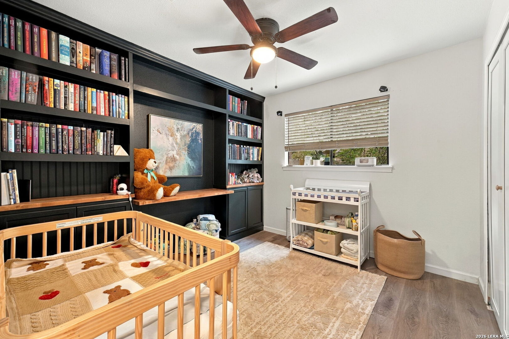 Nursery with a natural-wood crib, dark built-in bookshelves, and a changing table by the window.
