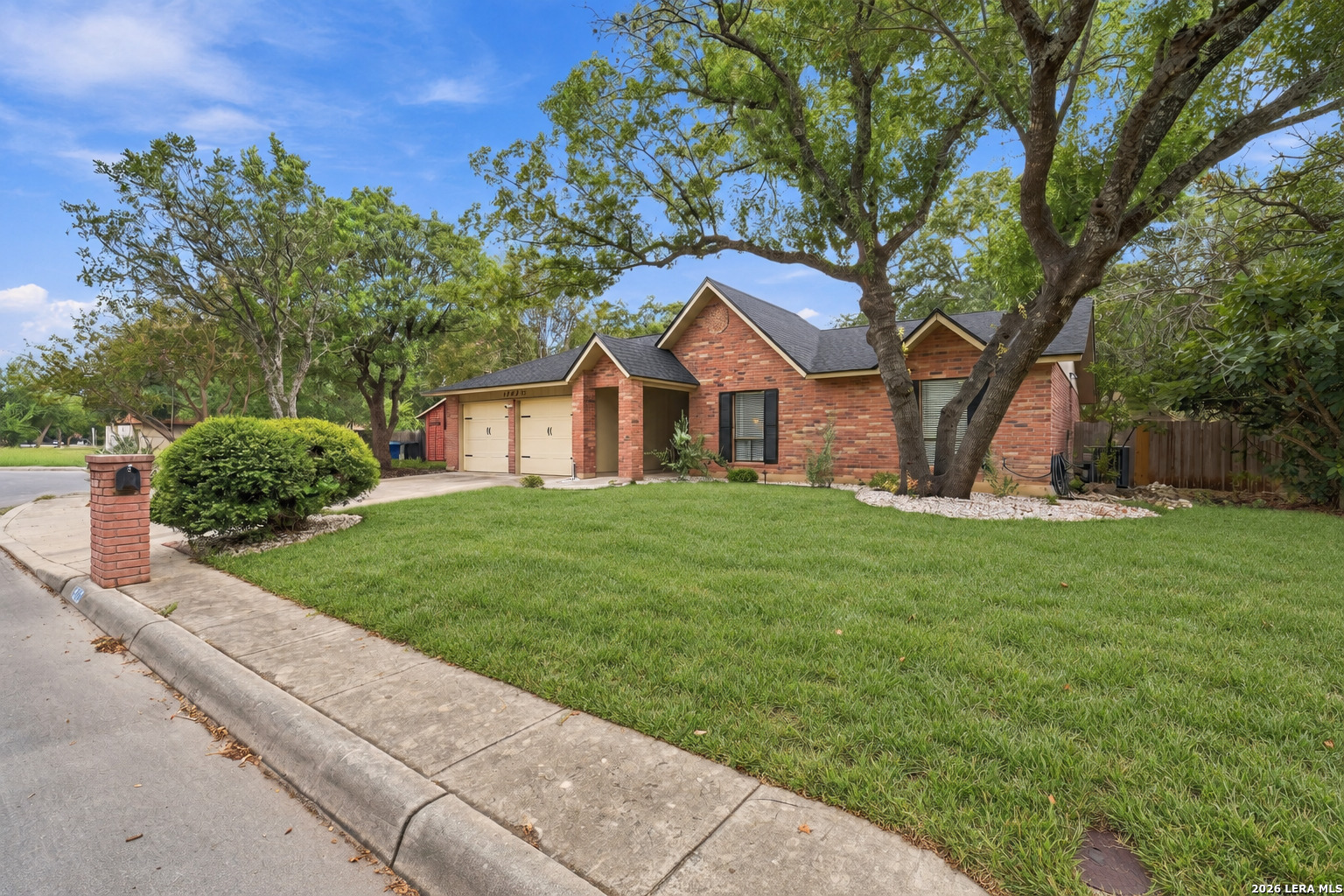 Red brick house with a two-car garage, mature shade trees, and a broad front lawn.
