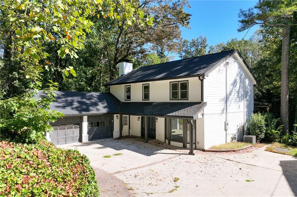 White two-story house with an attached garage, covered entry, and broad driveway among mature trees.