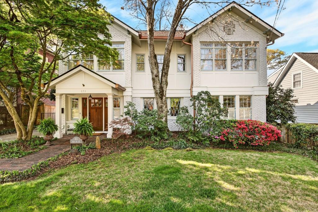 Two-story white brick home with a covered entry, mature trees, and landscaped front yard.