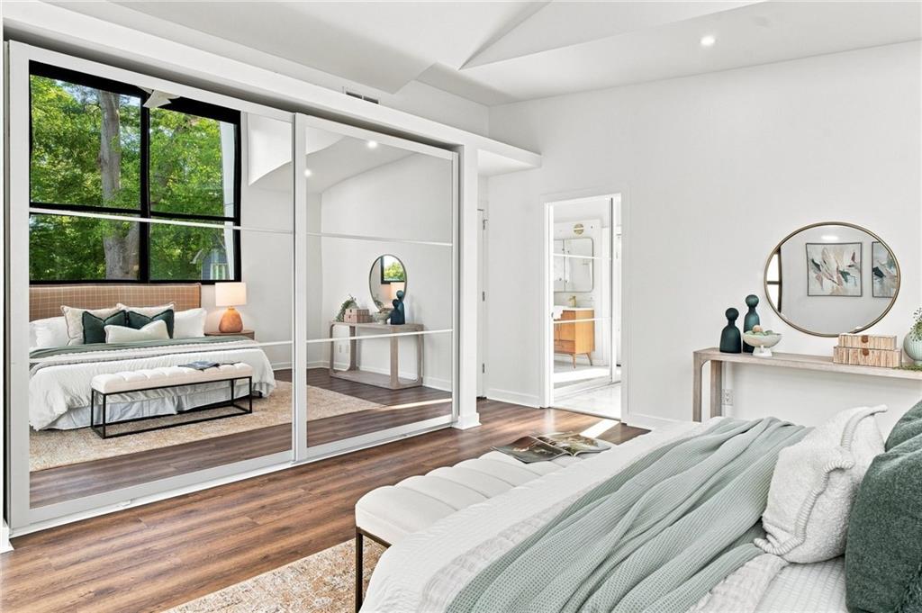 Staged bedroom with mirrored closet doors, large windows, and dark hardwood floors.