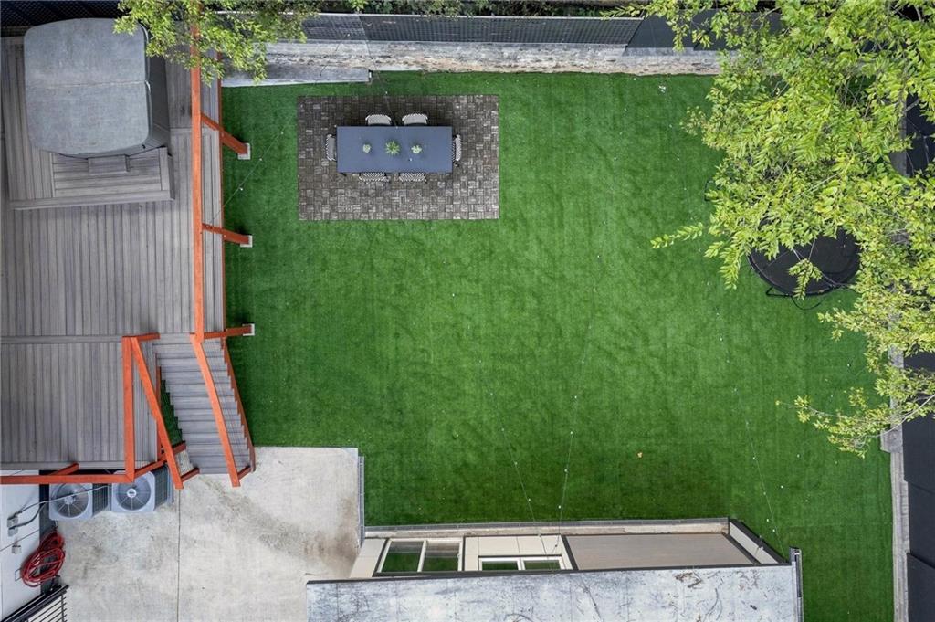 Aerial view of a backyard with a broad lawn, raised deck, and paved outdoor dining area.