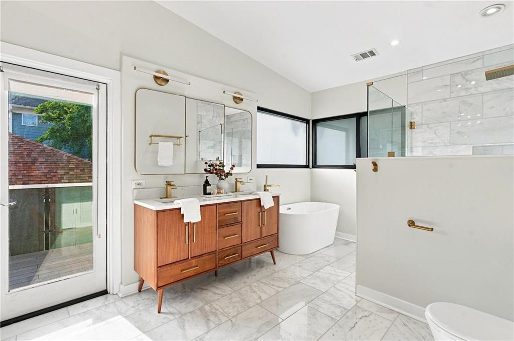 Bright bathroom with a wood double vanity, freestanding tub, and marble tile.