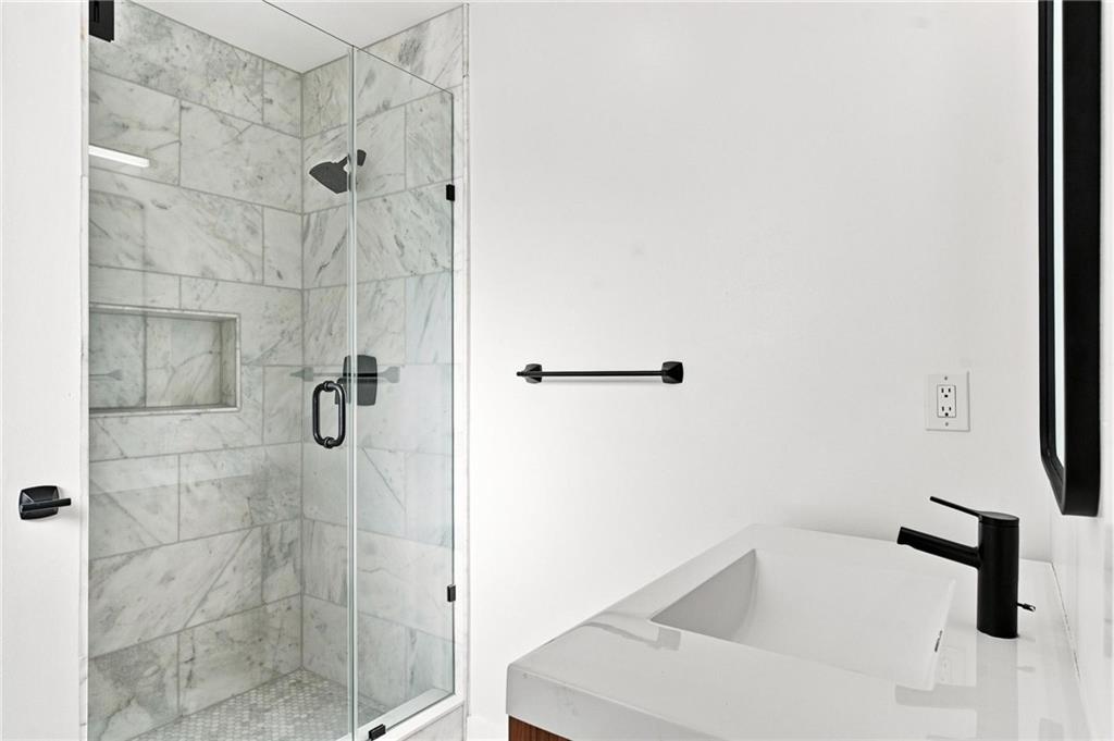 Modern bathroom with a marble-tiled glass shower and white vessel sink with black faucet.