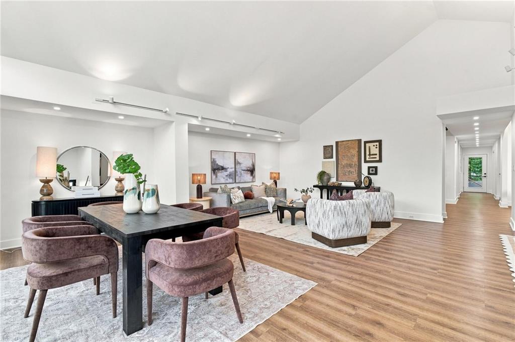 Staged living and dining room with a vaulted ceiling, wood floors, and a long hallway.