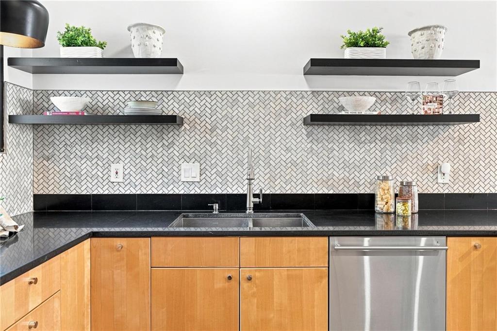 Modern kitchen with a geometric tile backsplash, black floating shelves, and light wood cabinets.