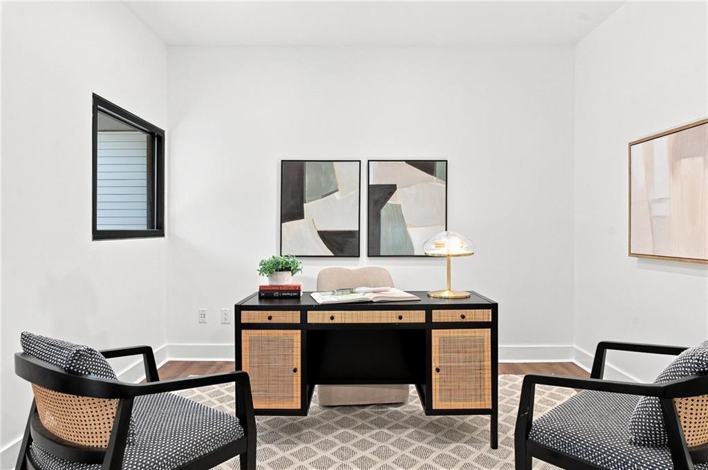 Staged home office with a cane-front desk, two chairs, abstract art, and a patterned rug.