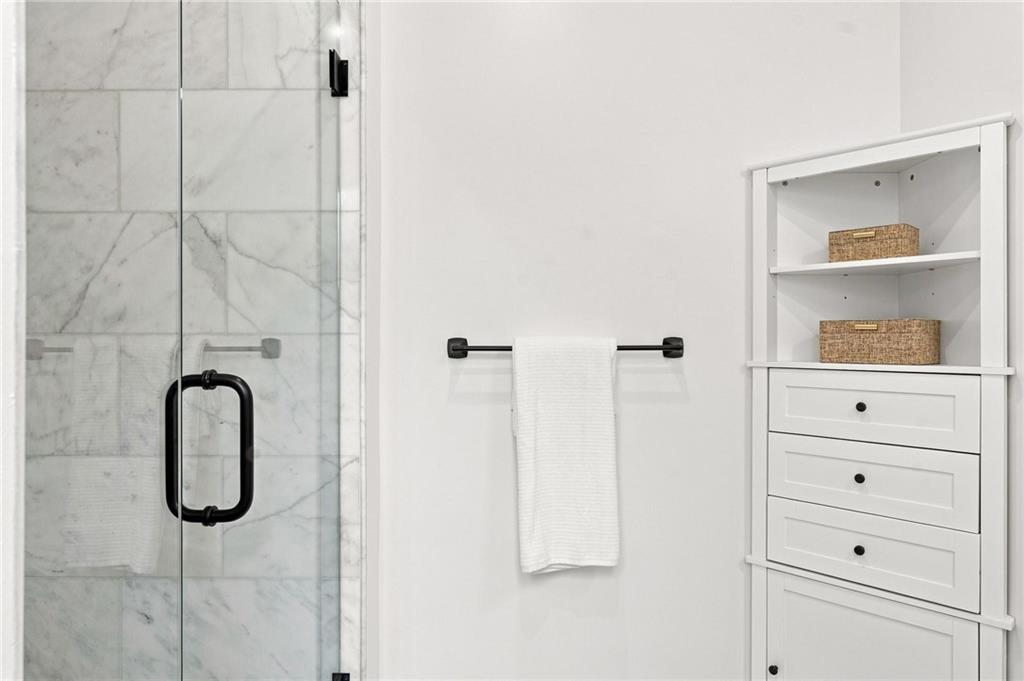 Bathroom with a marble-tiled glass shower, black fixtures, and a white cabinet with woven baskets.