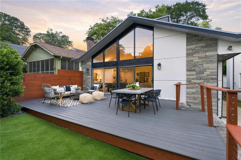Modern home with a broad deck, outdoor seating, floor-to-ceiling windows, and stone siding at sunset.