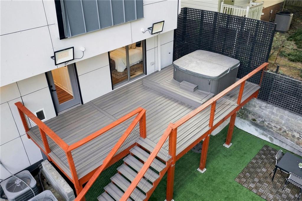 Elevated deck with a covered hot tub, gray composite decking, and orange railings.