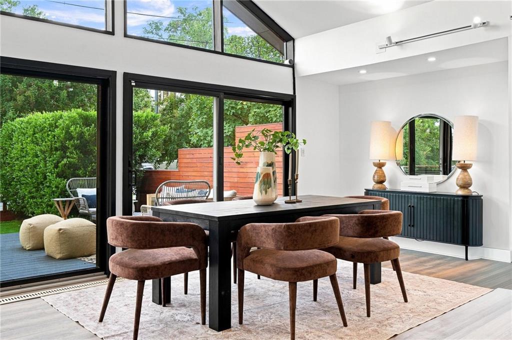 Dining room with brown upholstered chairs, a black table, and glass doors opening to a leafy patio.