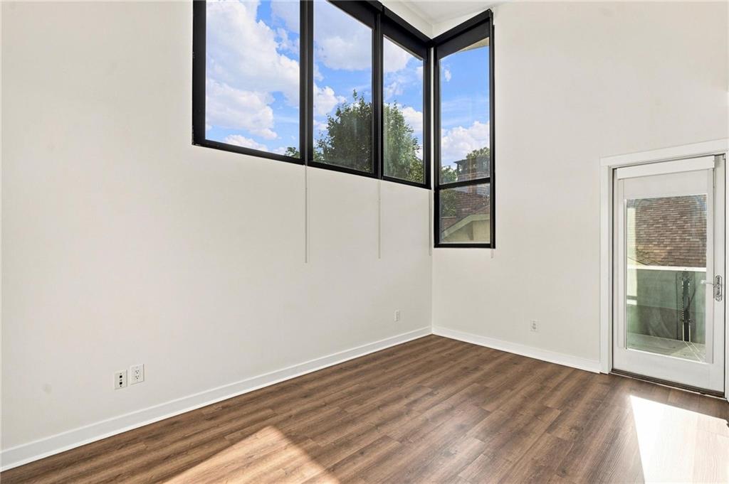 Empty room with tall black-framed windows, wood-look floors, and a glass balcony door.
