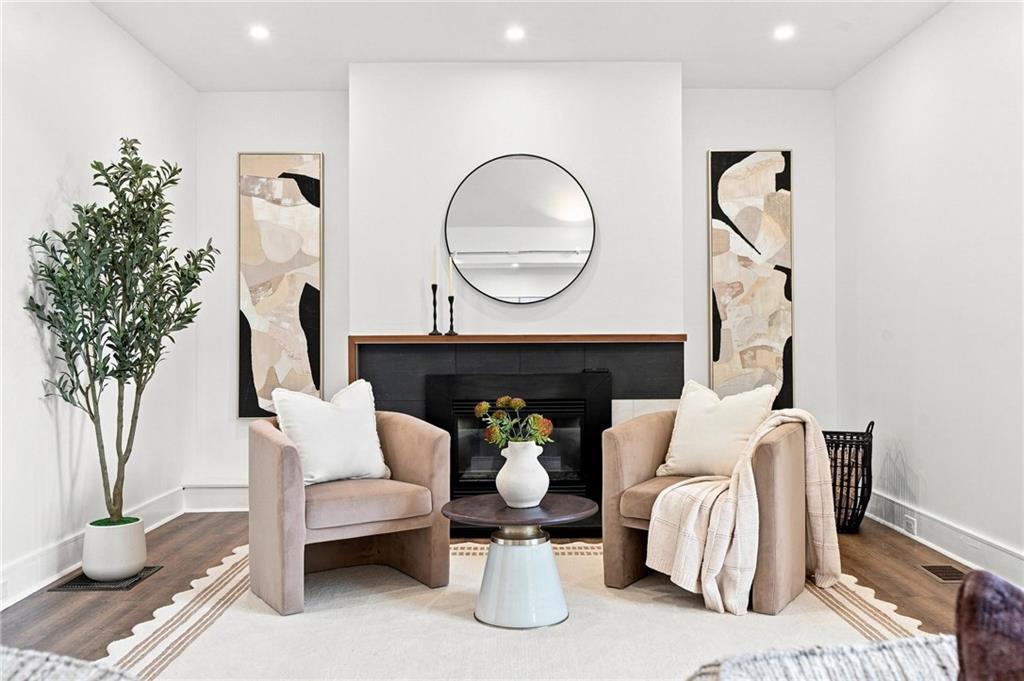 Staged living room with blush armchairs, a black fireplace, round mirror, and potted tree.