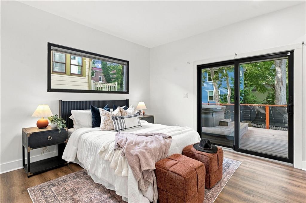 Furnished bedroom with a white bed, rust-colored ottomans, and sliding doors to a deck.