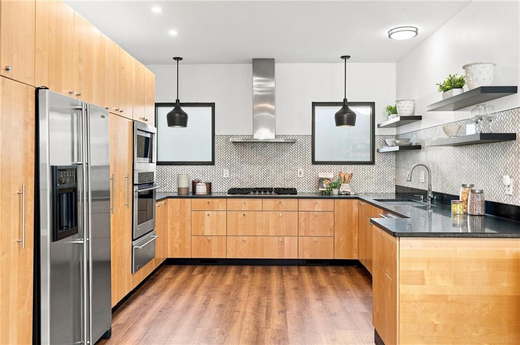 Modern kitchen with light wood cabinets, stainless steel appliances, and a large black-countertop island.