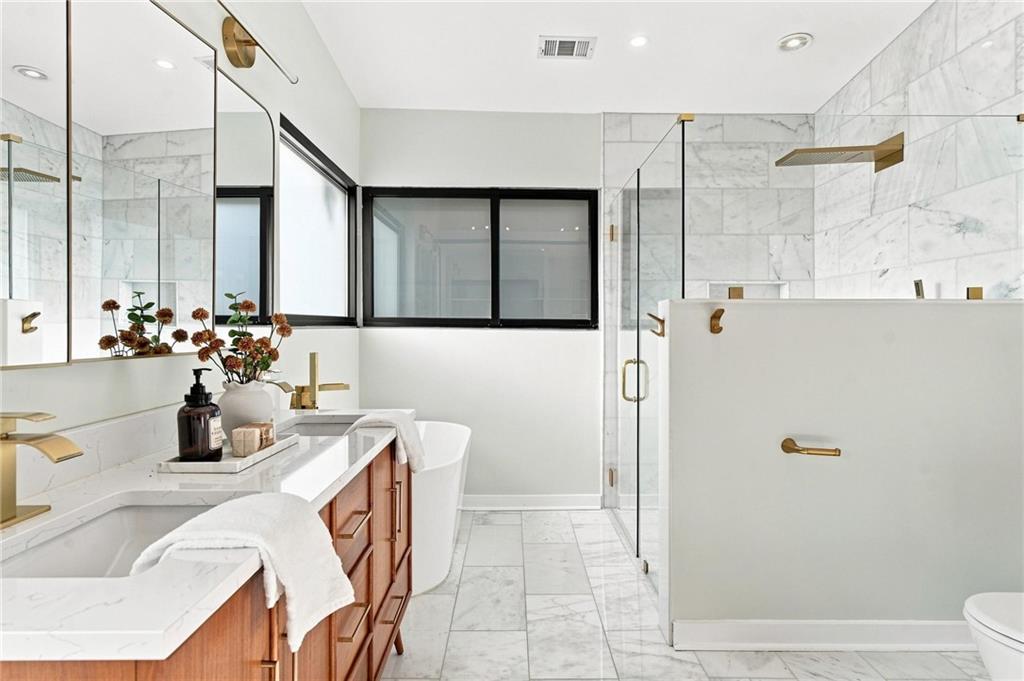 Marble bathroom with wood double vanity, freestanding tub, and glass shower with brass fixtures.