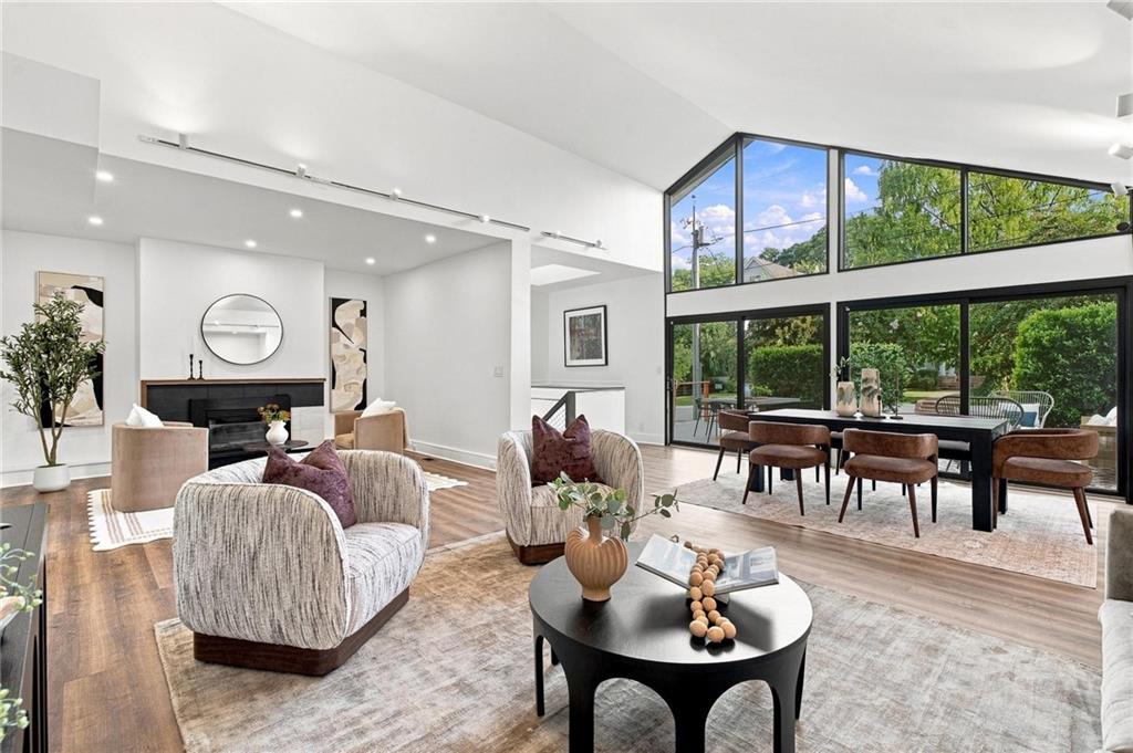 Open-plan living and dining room with vaulted ceilings, fireplace, and large windows overlooking greenery.