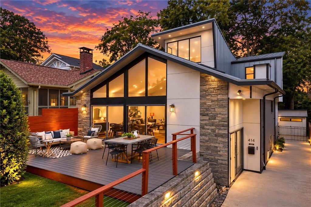 Modern home with stone accents and an illuminated, furnished deck at dusk.