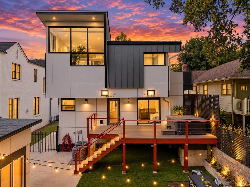 Modern home with illuminated windows, elevated deck, red stairs, and backyard lighting at dusk.